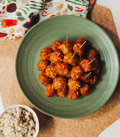 Pizza Sausage Barley Balls on toothpicks displayed on a green platter surrounded by linens and a bowl of cooked barley
