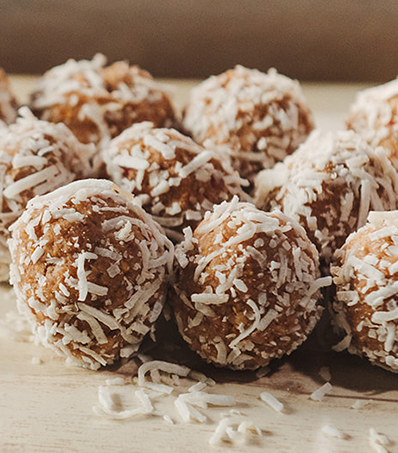 A close view of a tray of 12 energy balls rolled in shredded coconut.