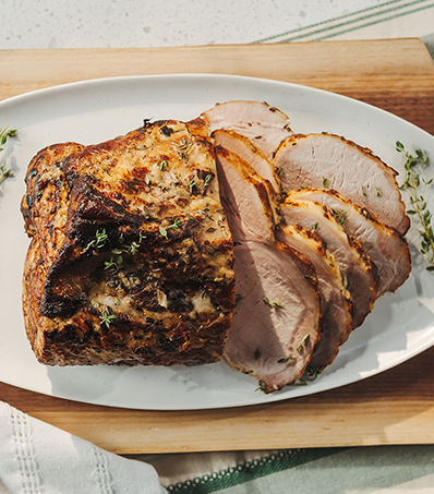 A sliced, cooked pork loin roast rests on a light oval plate. The roast is garnished with sprigs of thyme.
