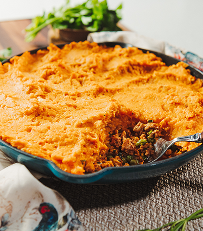 Ground chicken and pea stew in a blue skillet with a mashed sweet potato topping spread over the top, creating a skillet pie.