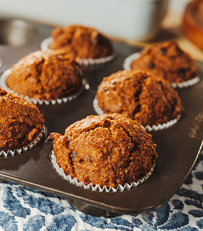 A muffin tray with 6 bran muffins on a blue and white patterned kitchen towel.